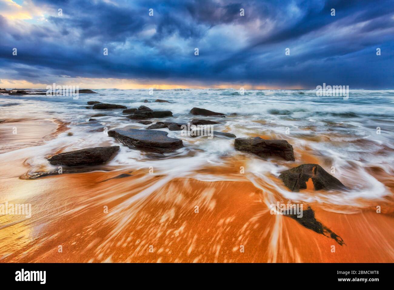 Spiaggia di sabbia con scure rocce arenaria all'alba sulle spiagge del Nord di Sydney dell'oceano Pacifico. Foto Stock