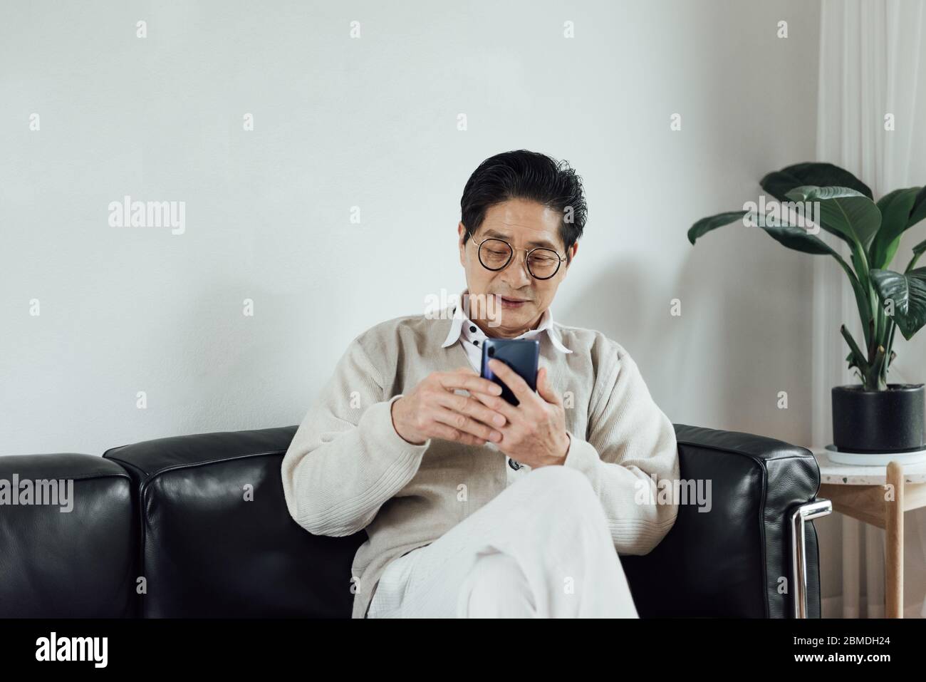 Un anziano asiatico che usa il telefono cellulare nel soggiorno Foto Stock