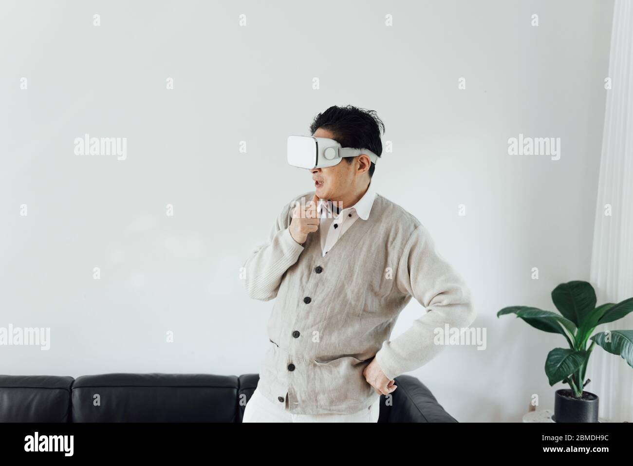 Un anziano asiatico che usa il telefono cellulare nel soggiorno Foto Stock