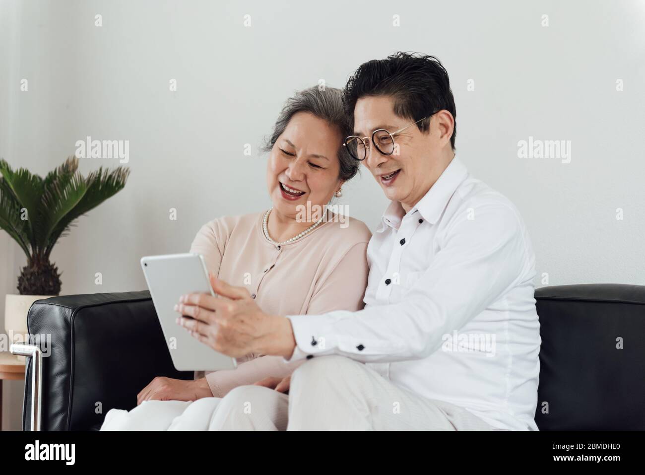 Una coppia asiatica anziana che usa dispositivi elettronici sul divano Foto Stock