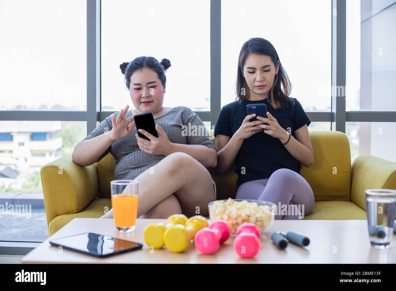 asian donna sovrappeso con amico giocare telefono cellulare e godere di mangiare cibo e popcorn sul divano a casa Foto Stock