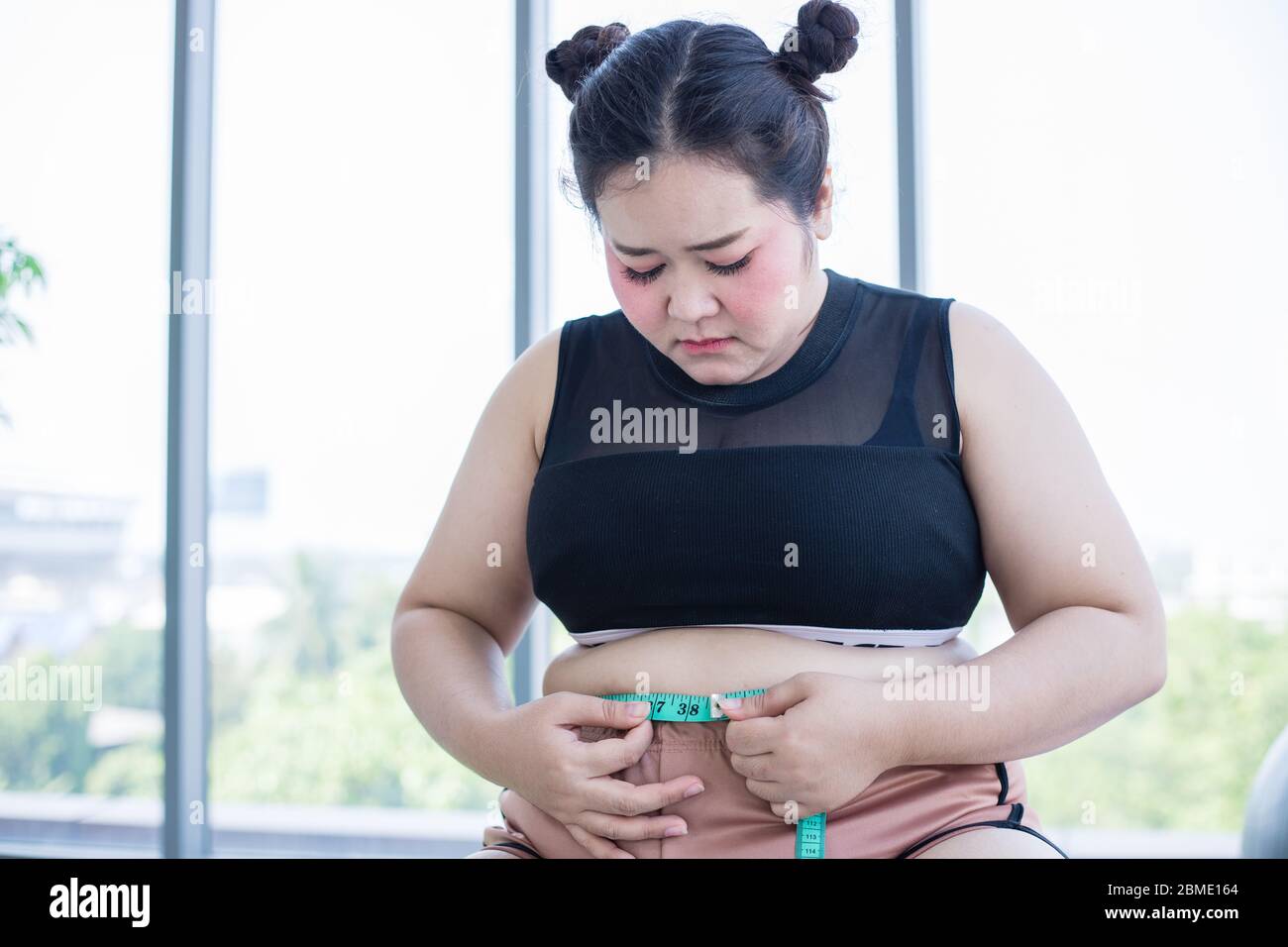 Donna in sovrappeso asiatico che misura lo strato grasso con la linea della vita a casa Foto Stock