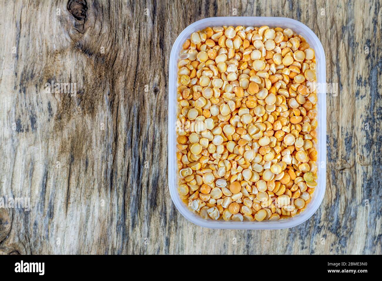 Piselli secchi crudi in contenitori di plastica su sfondo di legno Foto Stock