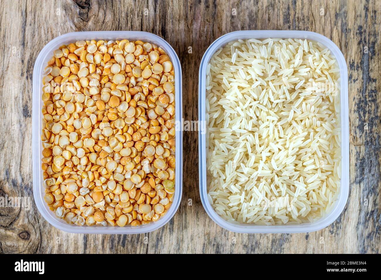 Riso crudo e piselli secchi in contenitori di plastica su fondo di legno Foto Stock