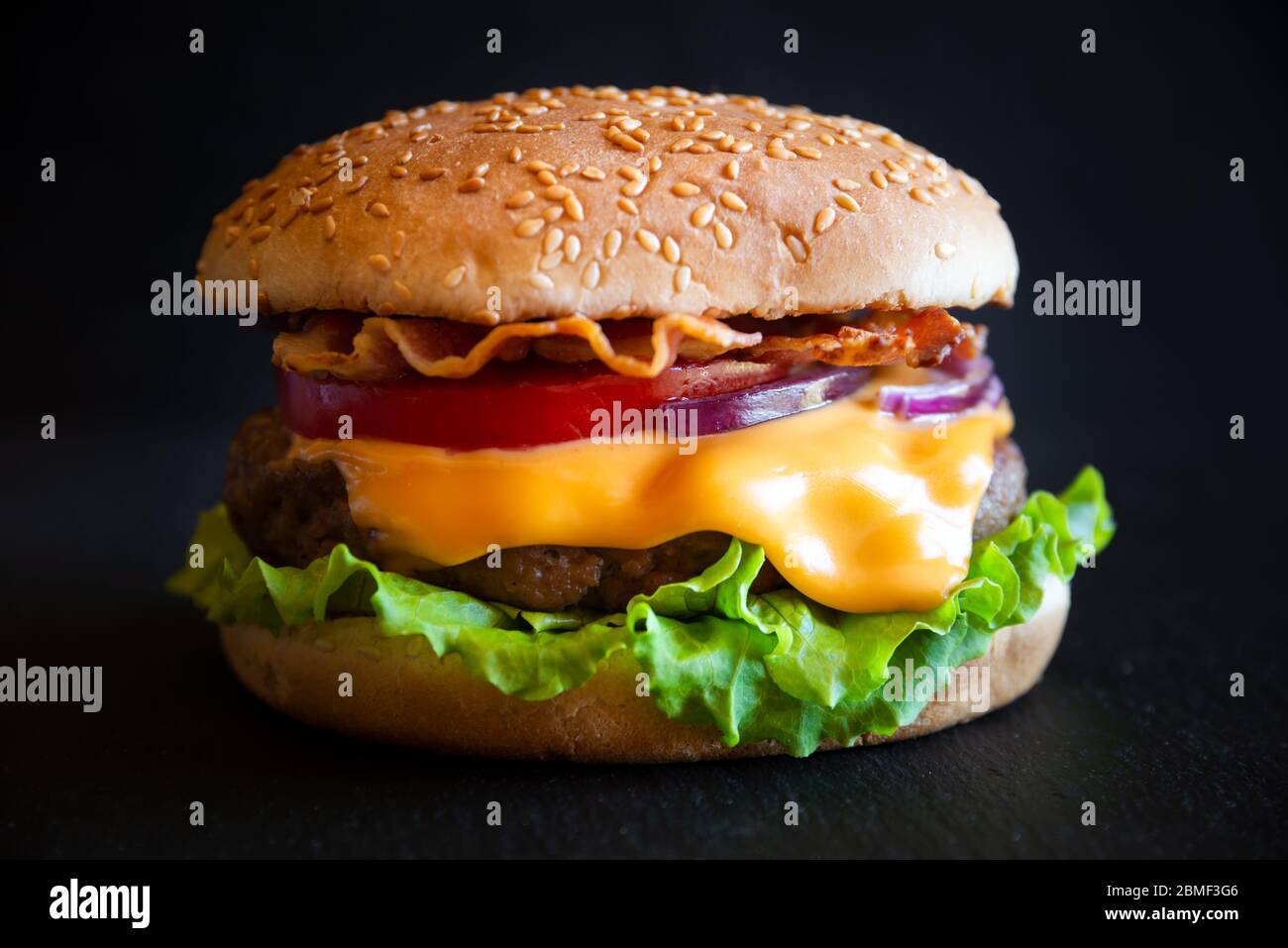 Hamburger con formaggio, pancetta, pomodoro e lattuga su fondo di legno scuro Foto Stock