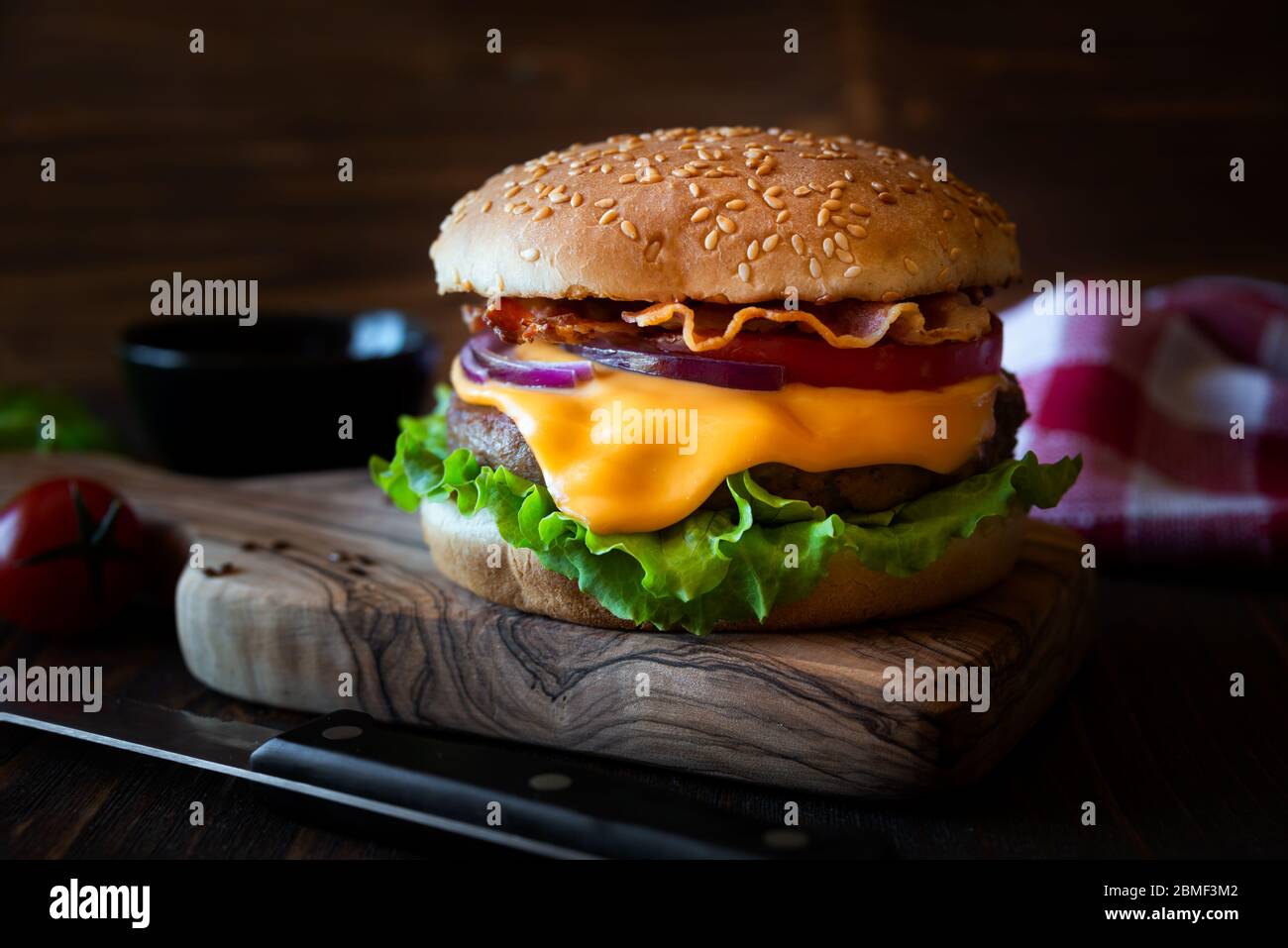 Hamburger con formaggio, pancetta, pomodoro e lattuga su fondo di legno scuro Foto Stock