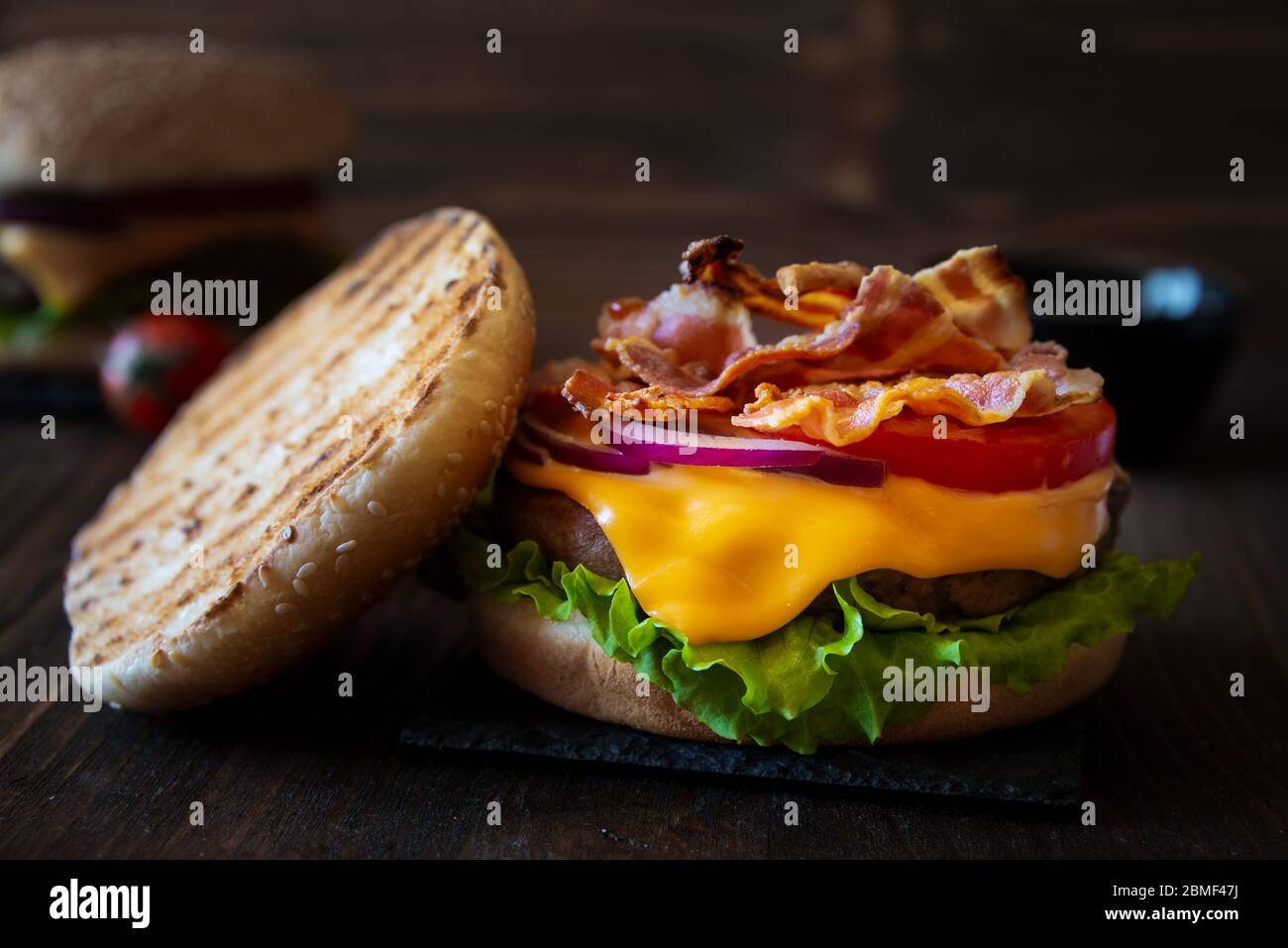 Hamburger con formaggio, pancetta, pomodoro e lattuga su fondo di legno scuro Foto Stock