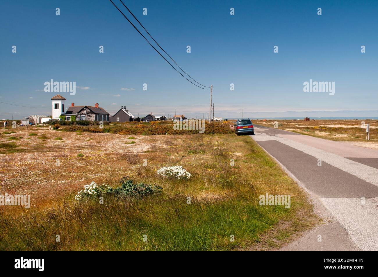 Dungeness, Inghilterra, Regno Unito - 8 giugno 2013: Una fila di case di legno basse è sparsa lungo la strada tra Dungeness e Lydd-on-Sea nel piano aspro envi Foto Stock