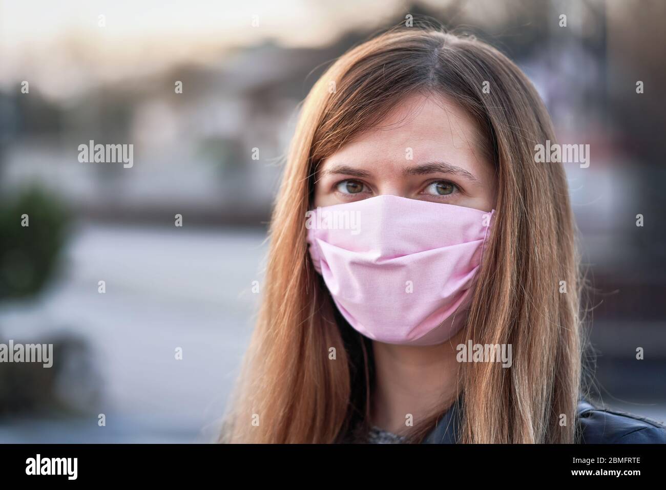 Giovane donna con mano rosa fatto in cotone faccia naso bocca maschera ritratto, sfocata città vuota dietro di lei. Può essere usato durante l'epidemia di coronavirus covid-19 Foto Stock