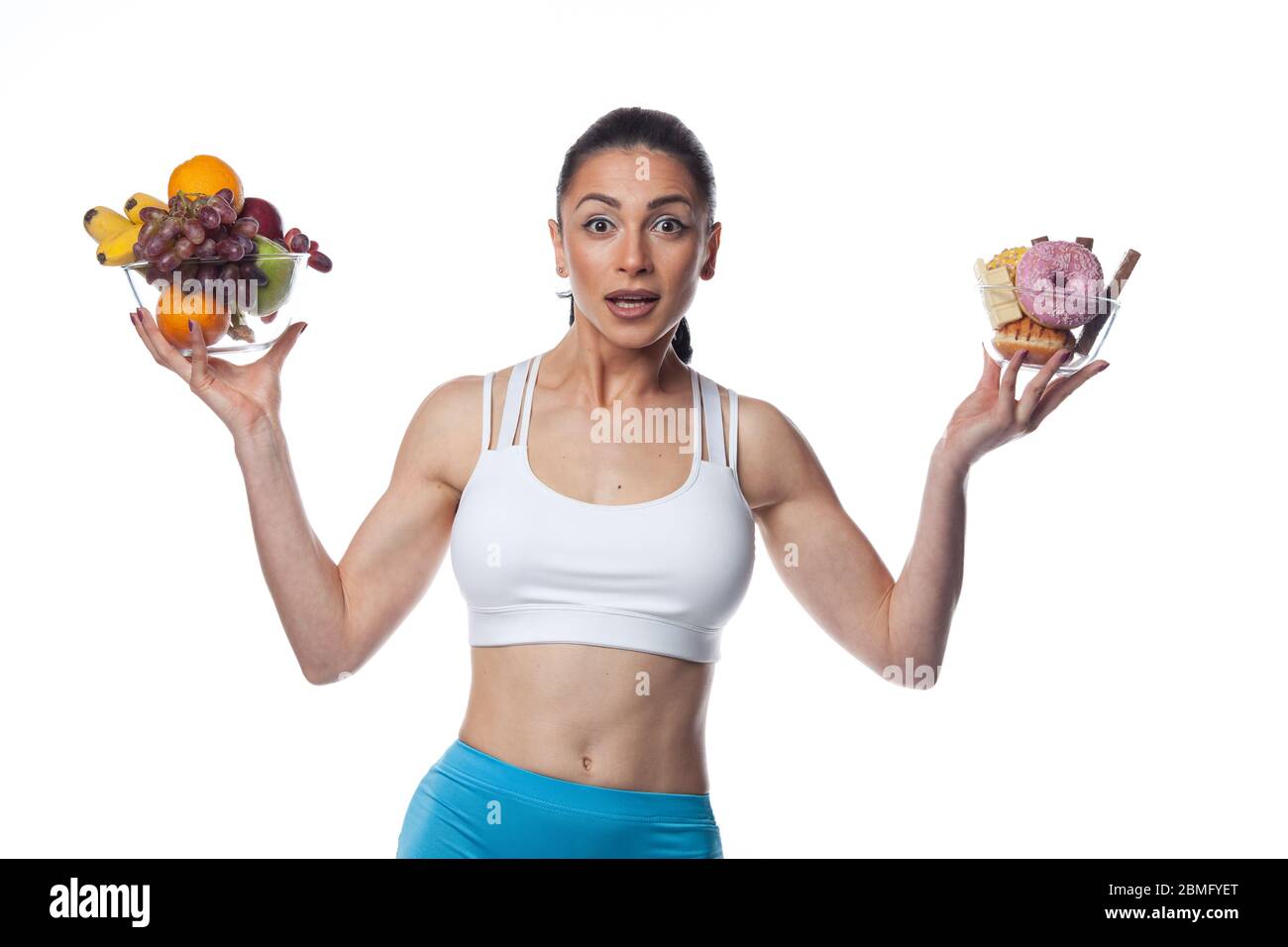 Donna bruna sexy in costume da fitness mangiare frutta e caramelle. Studio di ripresa isolato su sfondo bianco. Foto Stock