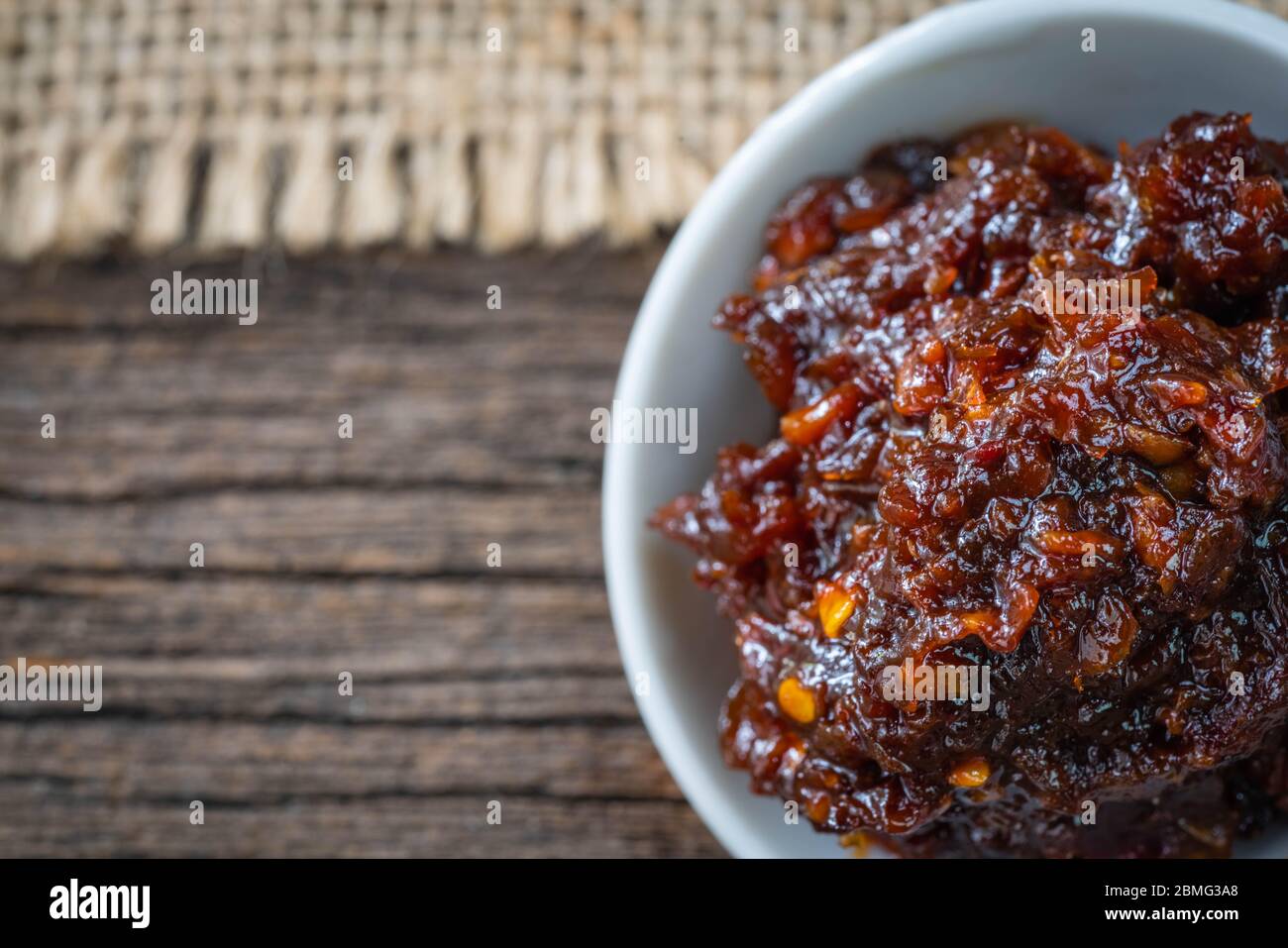 Pasta piccante di peperoncino in contenitore bianco in ceramica su fondo in legno Foto Stock