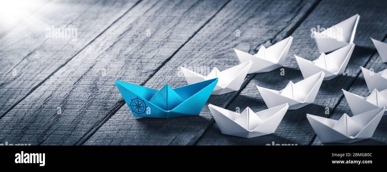 Blue Paper Boat alla guida di una flotta di piccole barche bianche con icona Bussola su tavola di legno con luce solare - concetto di leadership Foto Stock