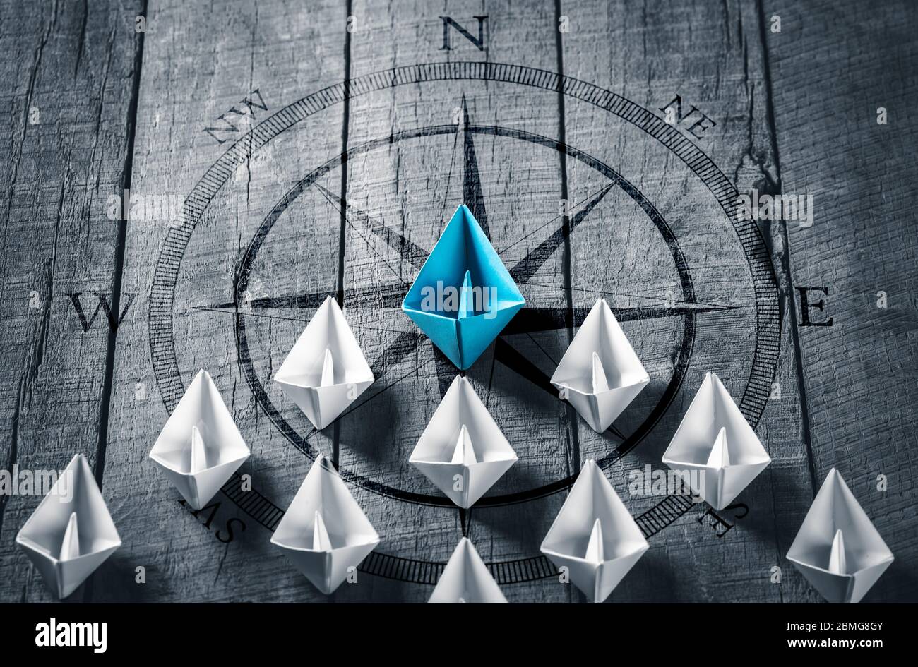 Blue Paper Boat alla guida di una flotta di piccole barche bianche con icona Bussola su tavola di legno con luce solare - concetto di leadership Foto Stock