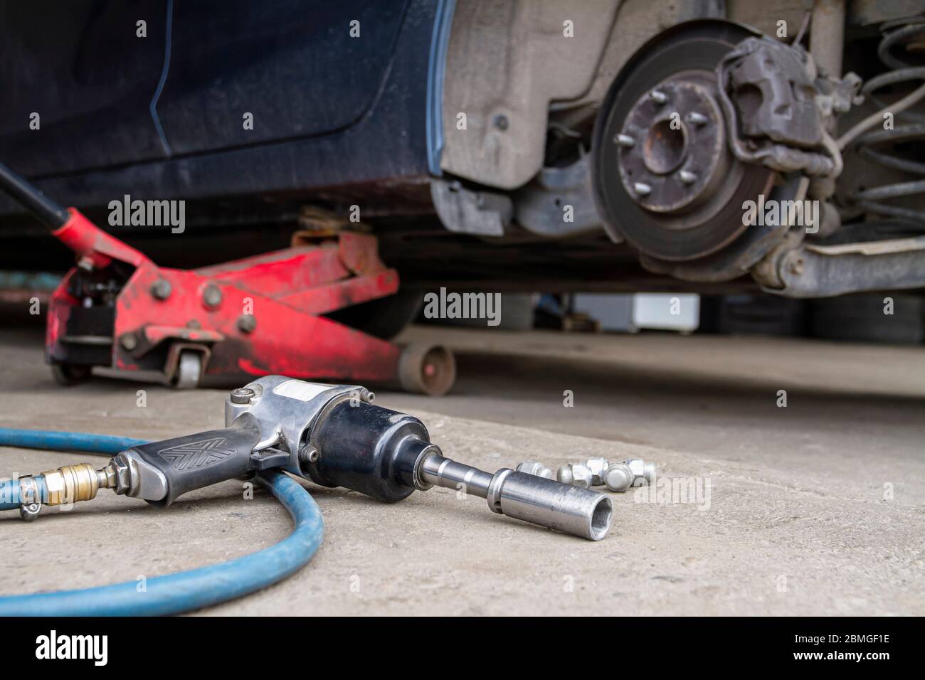 Chiave pneumatica sull'asfalto e martinetto per sollevare la carrozzeria e sostituire lo pneumatico. Auto senza ruota Foto Stock