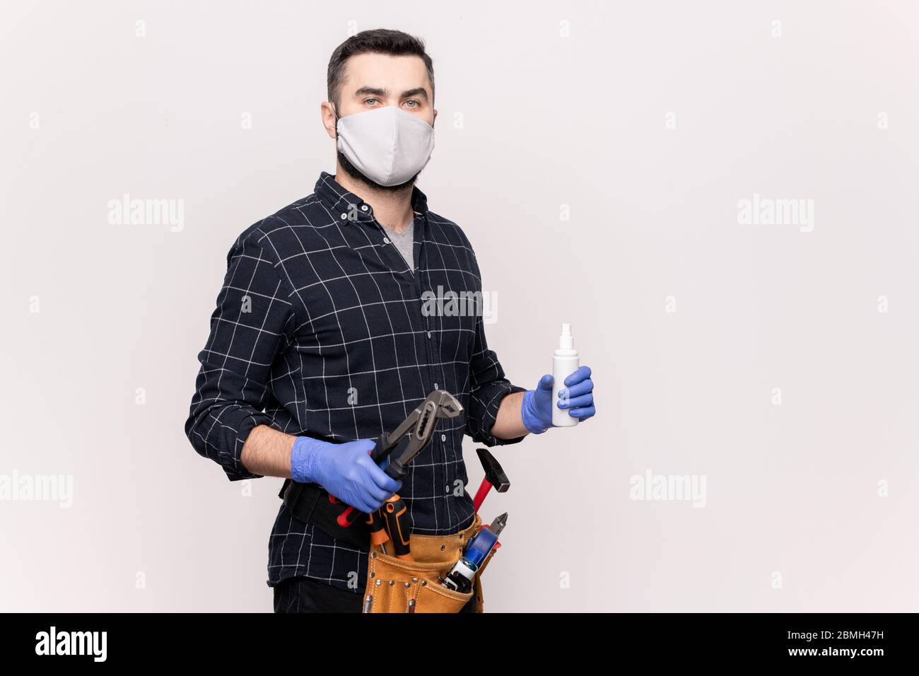 Giovane riparatore in maschera protettiva e guanti andare a riparare mobili o attrezzature idrauliche mentre si guarda in isolamento Foto Stock