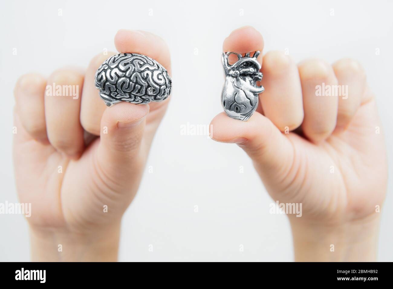 Primo piano di mani femminili che tengono copie anatomiche miniaturizzate del cuore umano e del cervello isolate su sfondo grigio. Emozioni contro logica. Foto Stock