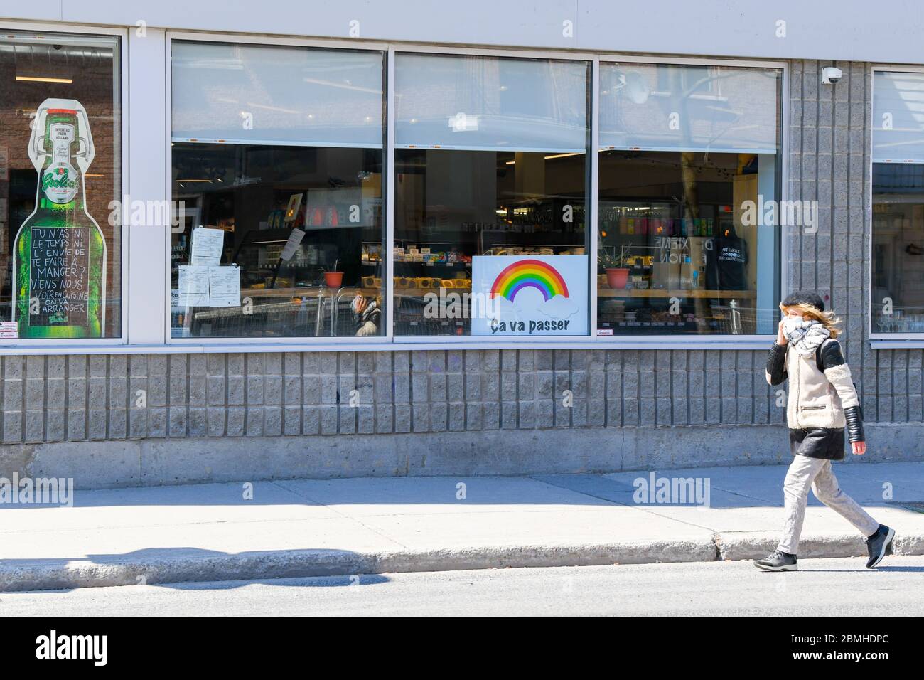 Persona che indossa una maschera protettiva e una sciarpa che cammina davanti ad un negozio con un covid 19 arcobaleno di speranza poster su di esso (il poster dice in francese: Passerà) , Montreal Canada Foto Stock