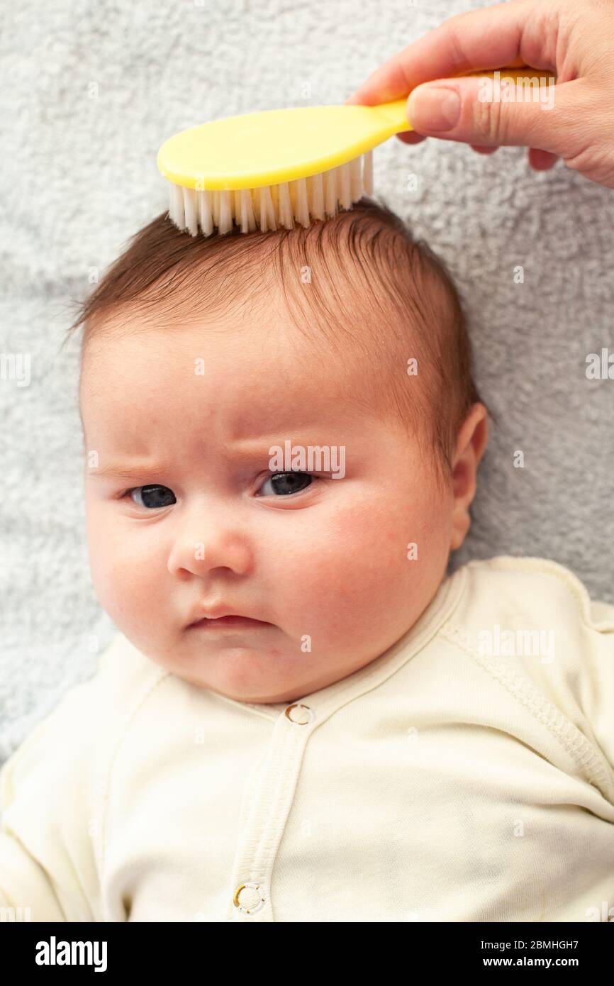 La mamma pettina un neonato con una speciale spazzola per capelli. Igiene del bambino Foto Stock