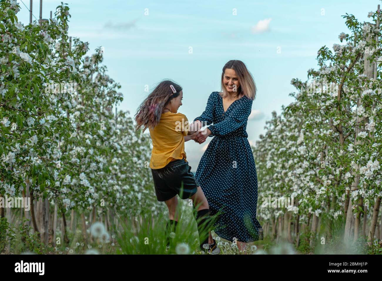 Felice mamma e figlia bella in abiti eleganti che ballano tra il giardino fiorente Foto Stock