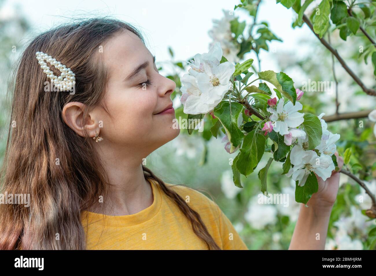 Ragazza bruna tenera con trucco naturale profumando ramo fiorente con occhi chiusi Foto Stock