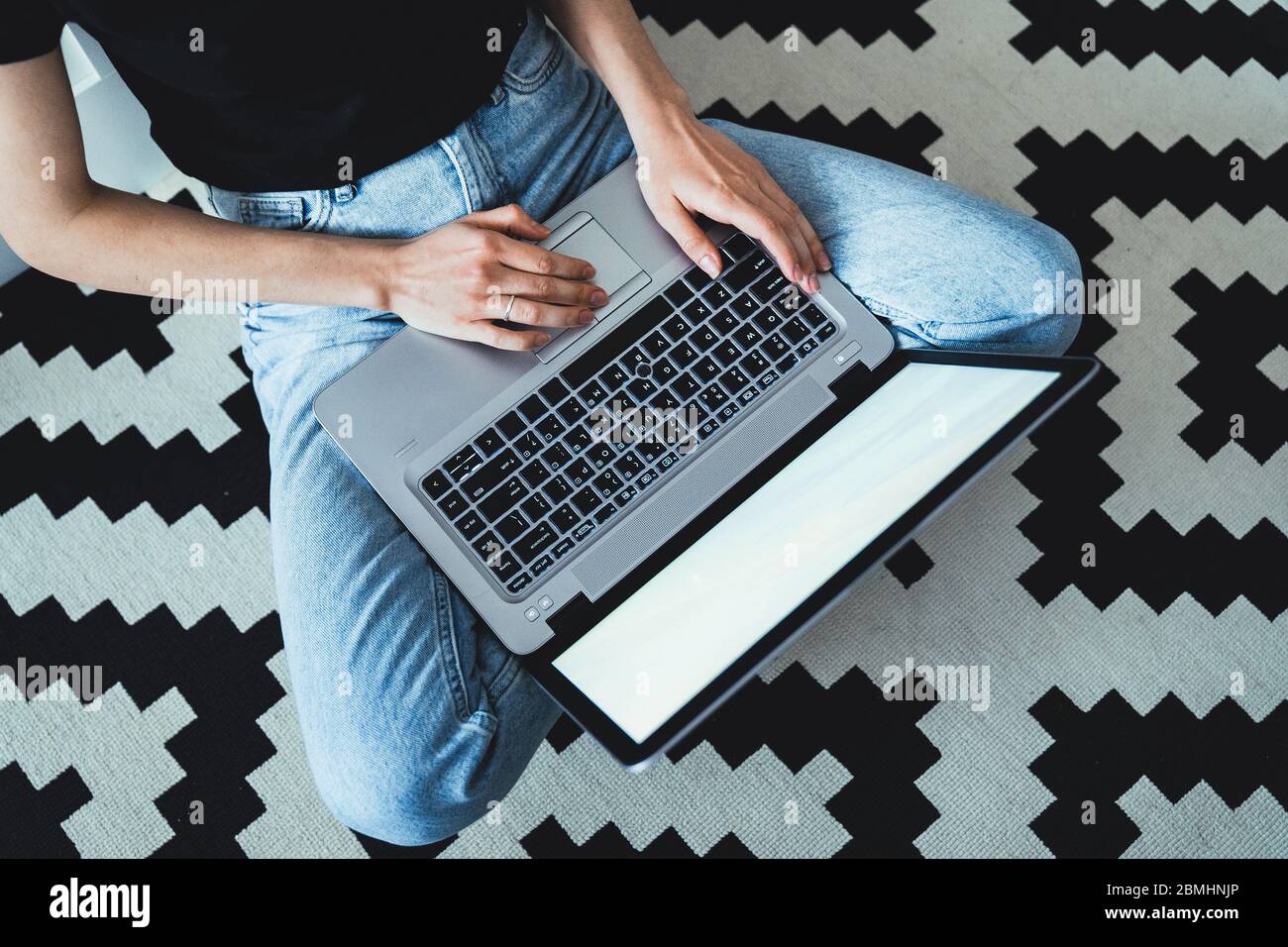 Concetto di casa lavorativa - ragazza seduta sul pavimento mentre lavora al laptop. Foto Stock