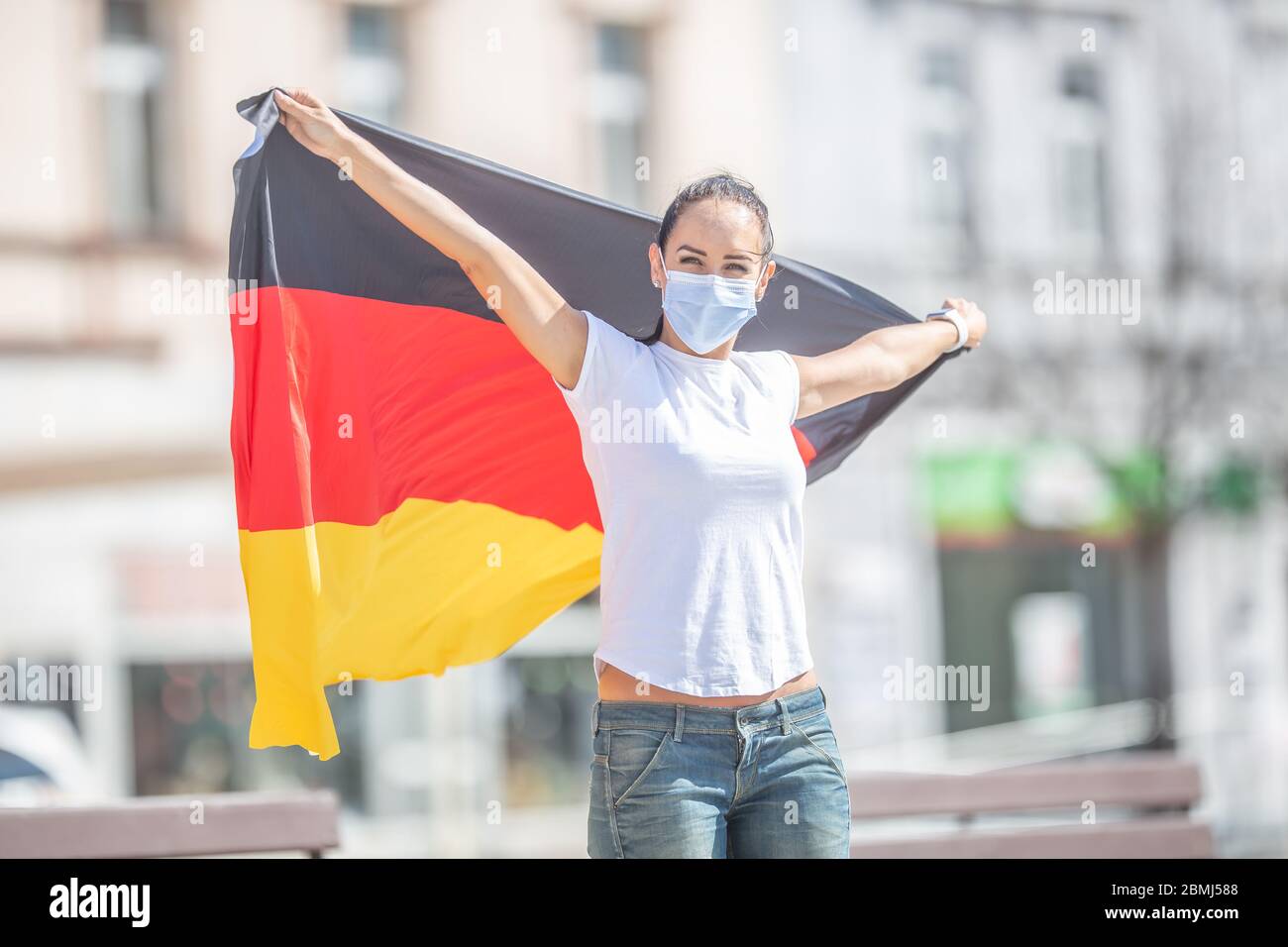Il fan tedesco in una maschera facciale tiene la bandiera dietro di lei all'aperto, sorridendo. Foto Stock