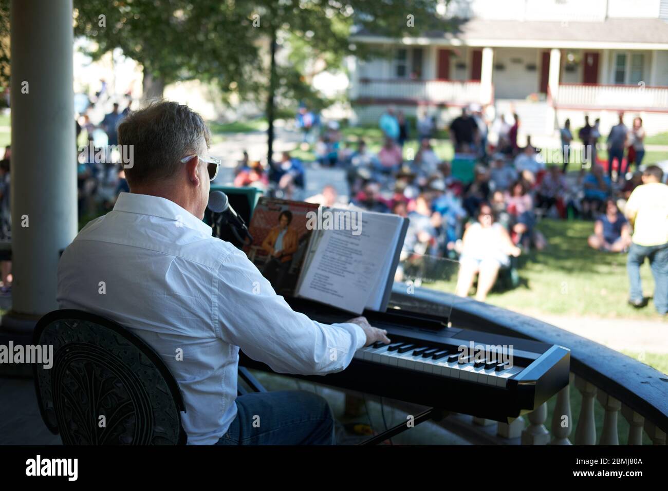 Uomo che indossa una camicia bianca e suona una tastiera elettrica per pianoforte a una folla all'aperto in un concerto estivo in un quartiere residenziale storico Foto Stock