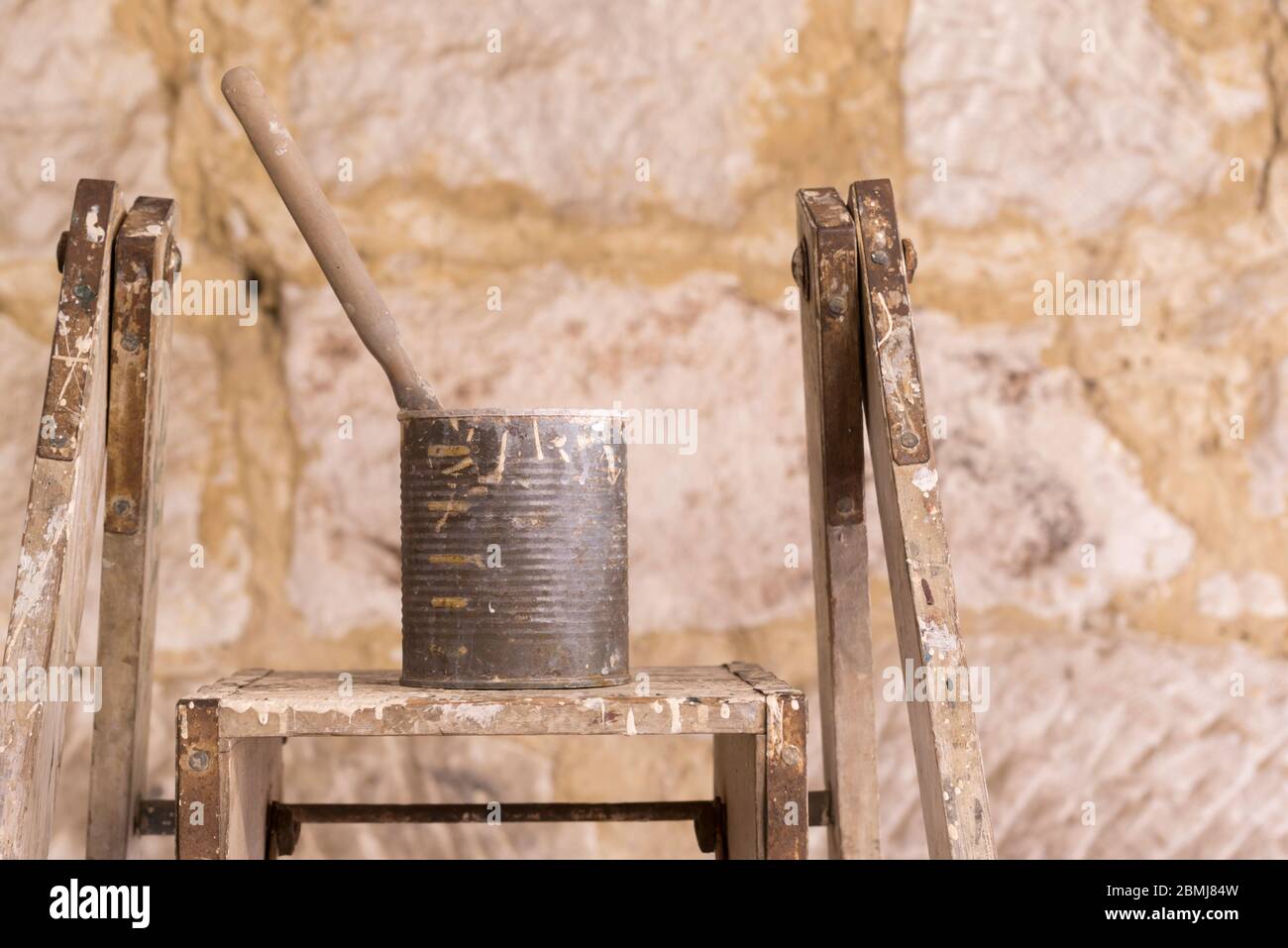 Un unico pennello seduta in una vecchia lattina di frutta in scatola coperta di vernice e poggiante su una vecchia scala dei pittori alla luce del sole del mattino Foto Stock