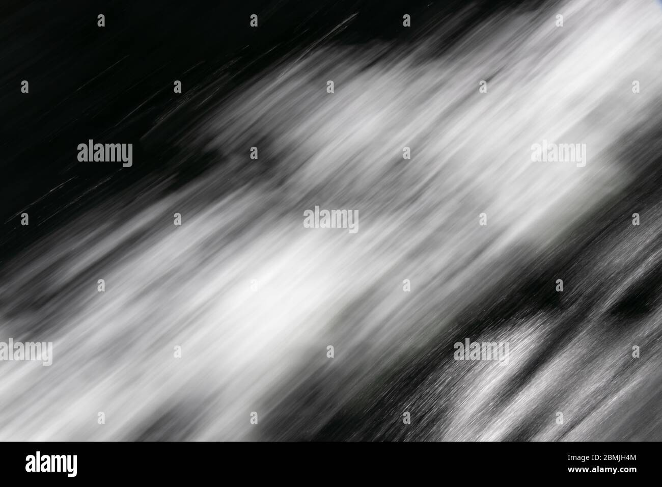 Movimento immagine in bianco e nero sfocata di acqua in rapido movimento evidenziata con luce solare intensa, che richiama la sensazione di movimento e velocità Foto Stock