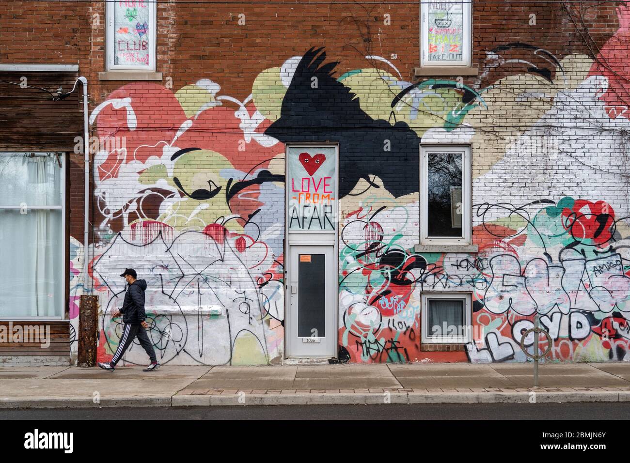 Toronto, Canada, l'uomo locale che indossa maschera facciale cammina di fronte a parete colorata con segni a tema di distanza sociale durante la pandemia di coronavirus. Foto Stock