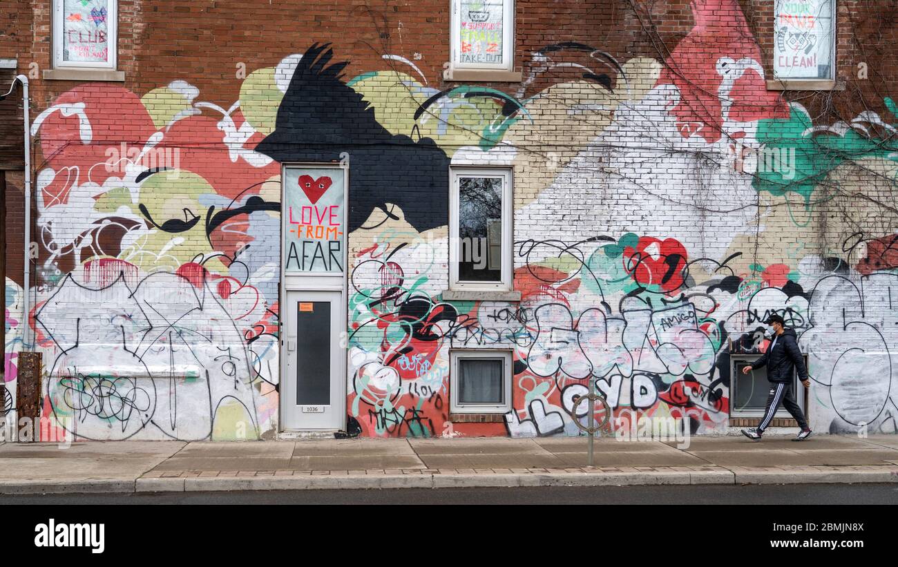 Toronto, Canada, uomo locale che indossa maschera facciale camminare di fronte a parete colorata con segni a tema di distanza sociale durante la pandemia coronavirus. Foto Stock