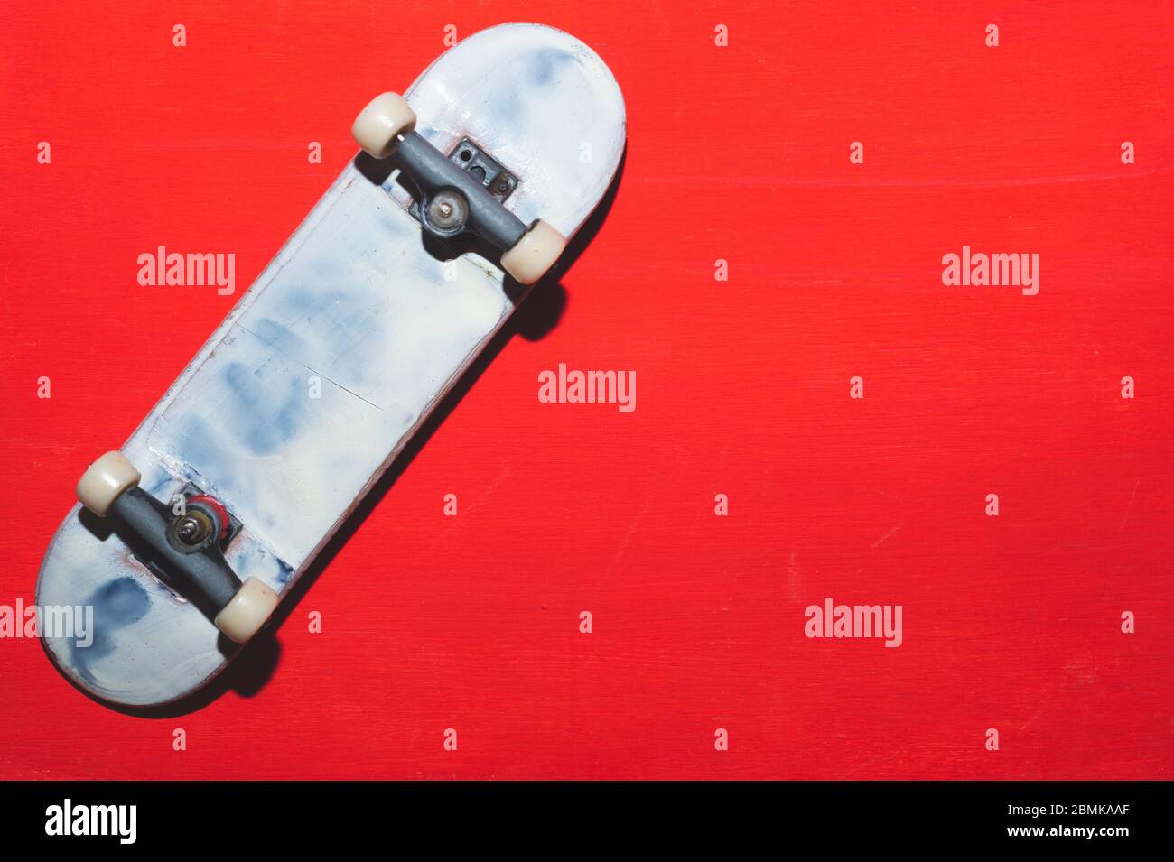 Skateboard piccola su sfondo rosso. Skate minuscolo per le dita. Primo piano per la tastiera. Spazio per la copia Foto Stock