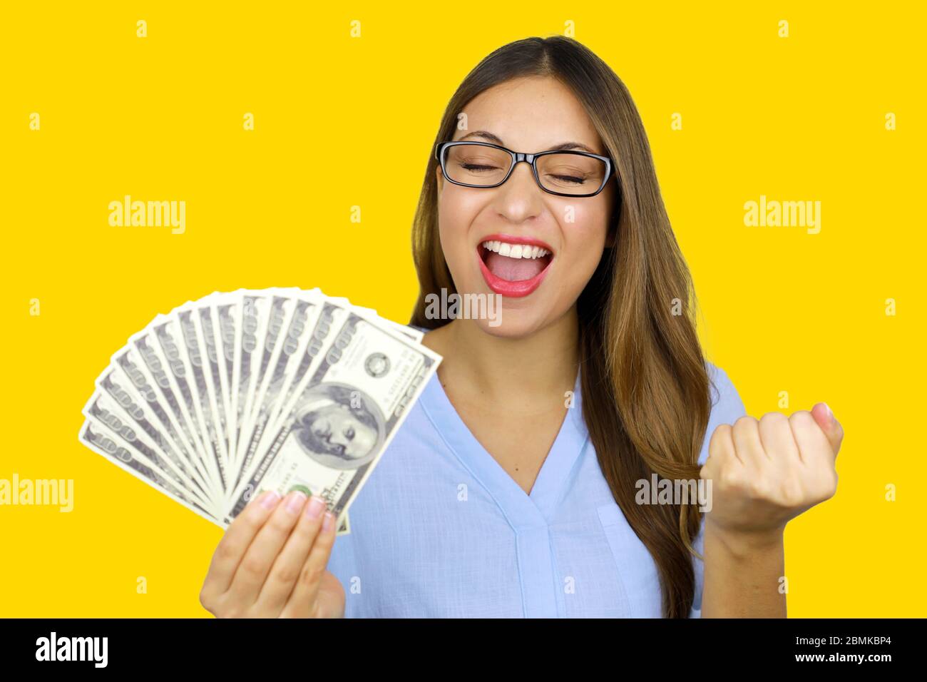 Ritratto di bella giovane donna ridendo e tenendo banconote in dollari isolato su sfondo giallo in studio. Concetto di prestiti facile. Foto Stock