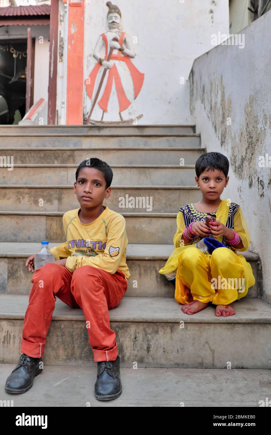 Un ragazzo indiano vestito con intelligenza e sua sorella minore seduto sui gradini del tempio Balaji al sacro carro armato di Banganga, Walkeshwar, Mumbai, India Foto Stock