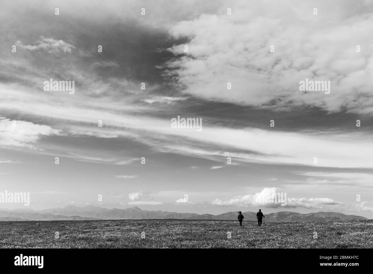 Due persone lontane camminano su un prato in primavera, sotto un grande cielo profondo Foto Stock