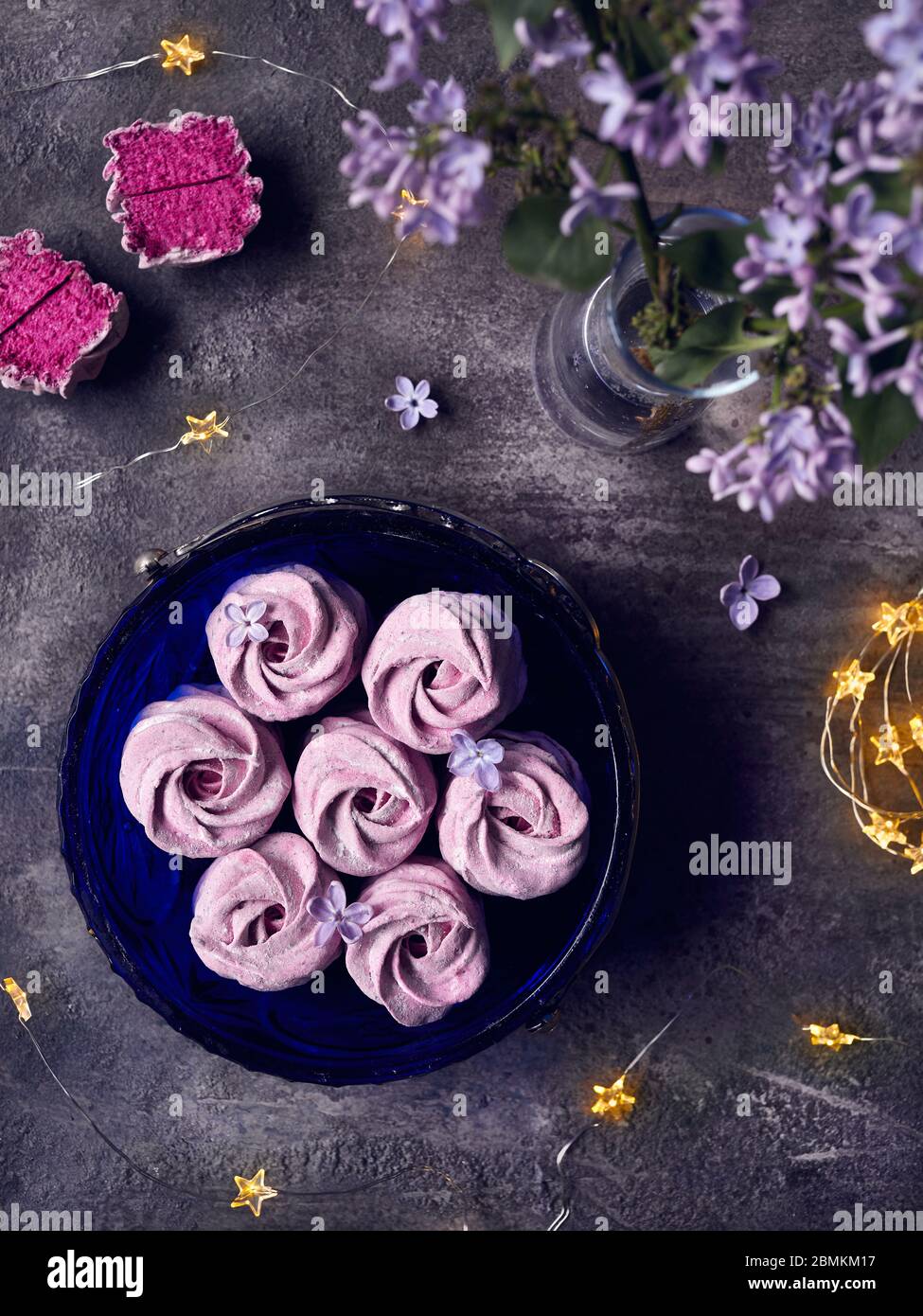 Atmosfera viola dolce fatto in casa Zephyr o Marshmallow da ribes nero vicino ai fiori lilla e magiche stelle luci su sfondo scuro vista dall'alto Foto Stock