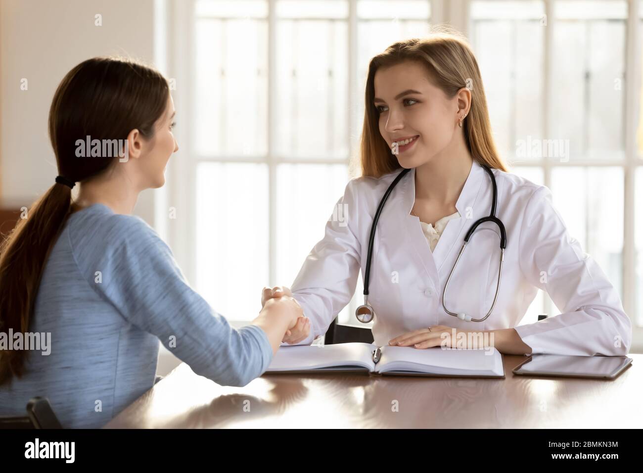 Sorridente medico stretta di mano donna paziente a consultazione Foto Stock