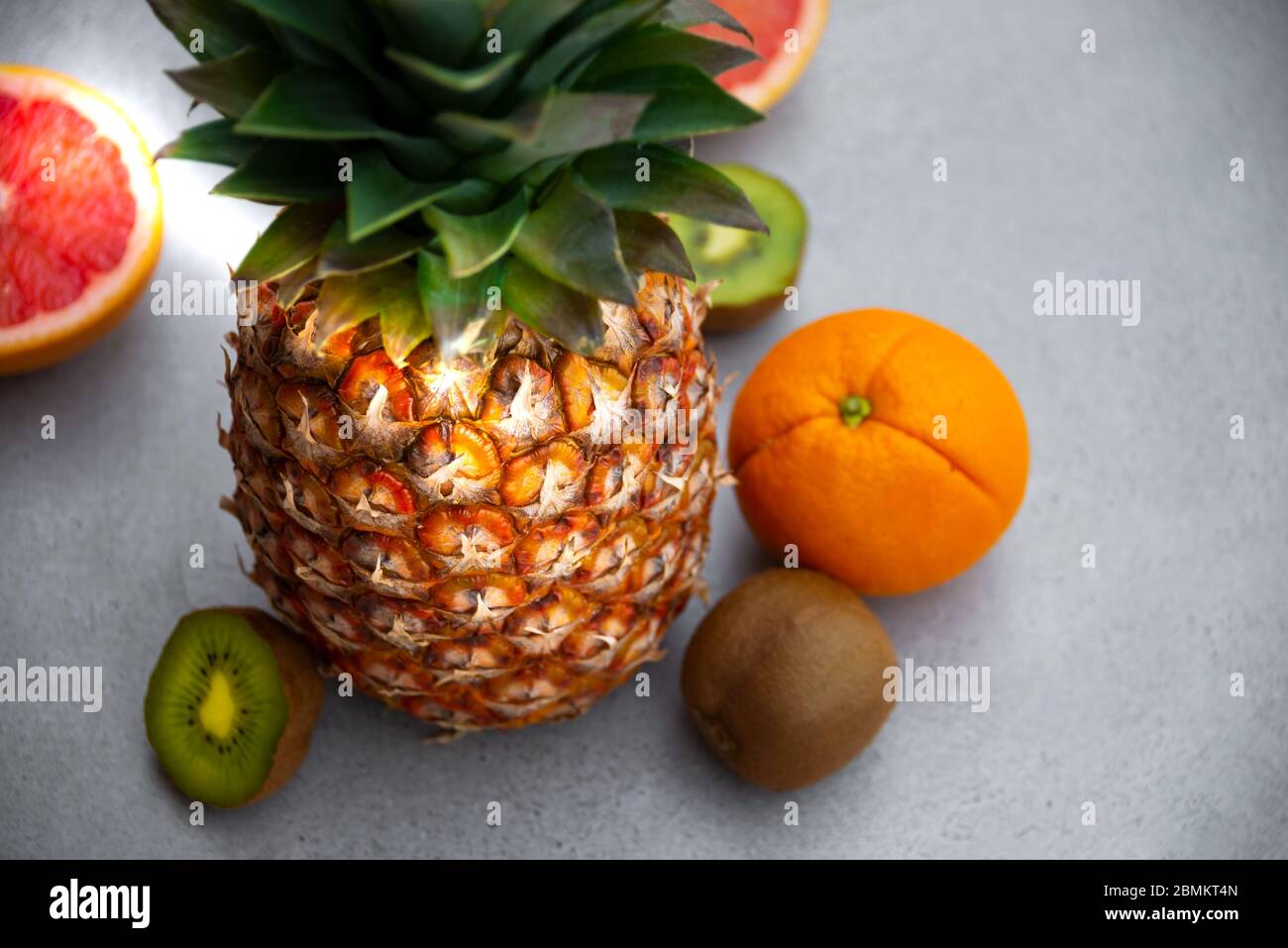 Ananas maturo e altri frutti - arancia, kiwi, pompelmo su sfondo grigio Foto Stock