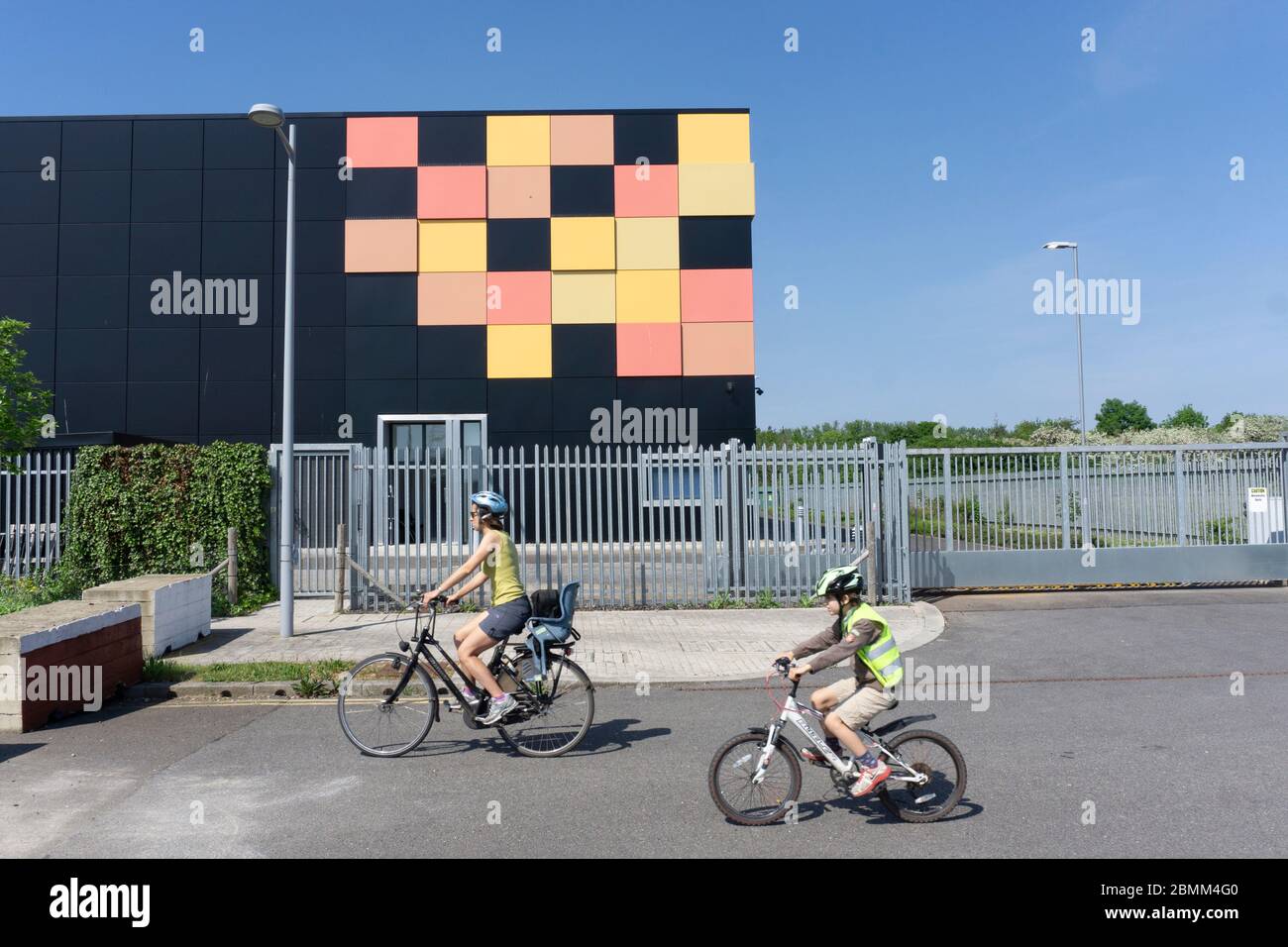 Edificio cubico nero opaco con piastrelle gialle e rosse in un angolo come design grafico dietro le ringhiere di sicurezza in metallo, data center cielo blu intenso Foto Stock