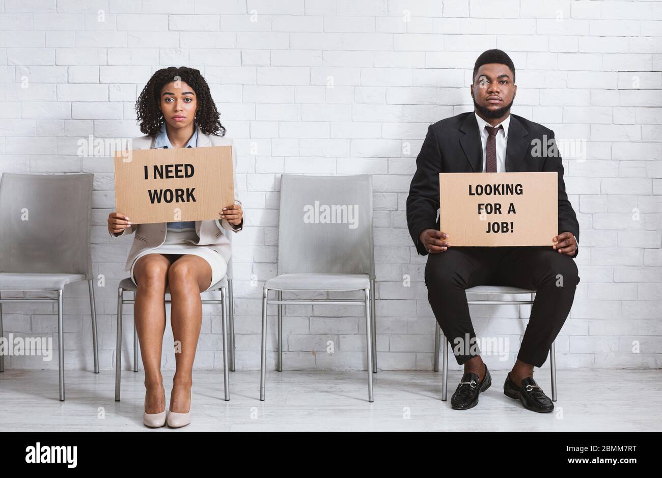 Ragazzo e ragazza Africano-americana con segni di cartone in attesa di intervista di lavoro in sala aziendale Foto Stock