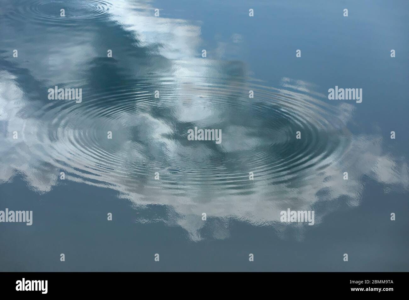 Riflesso di nuvola e cielo blu su specchio acqua liscia. I cerchi concentrici definiscono la superficie dell'acqua Foto Stock