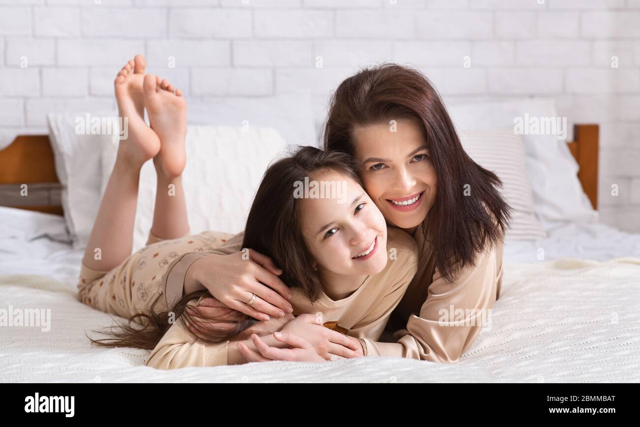 Amore del bambino del genitore. Giovane donna abbracciando la figlia adolescente a letto, panorama Foto Stock