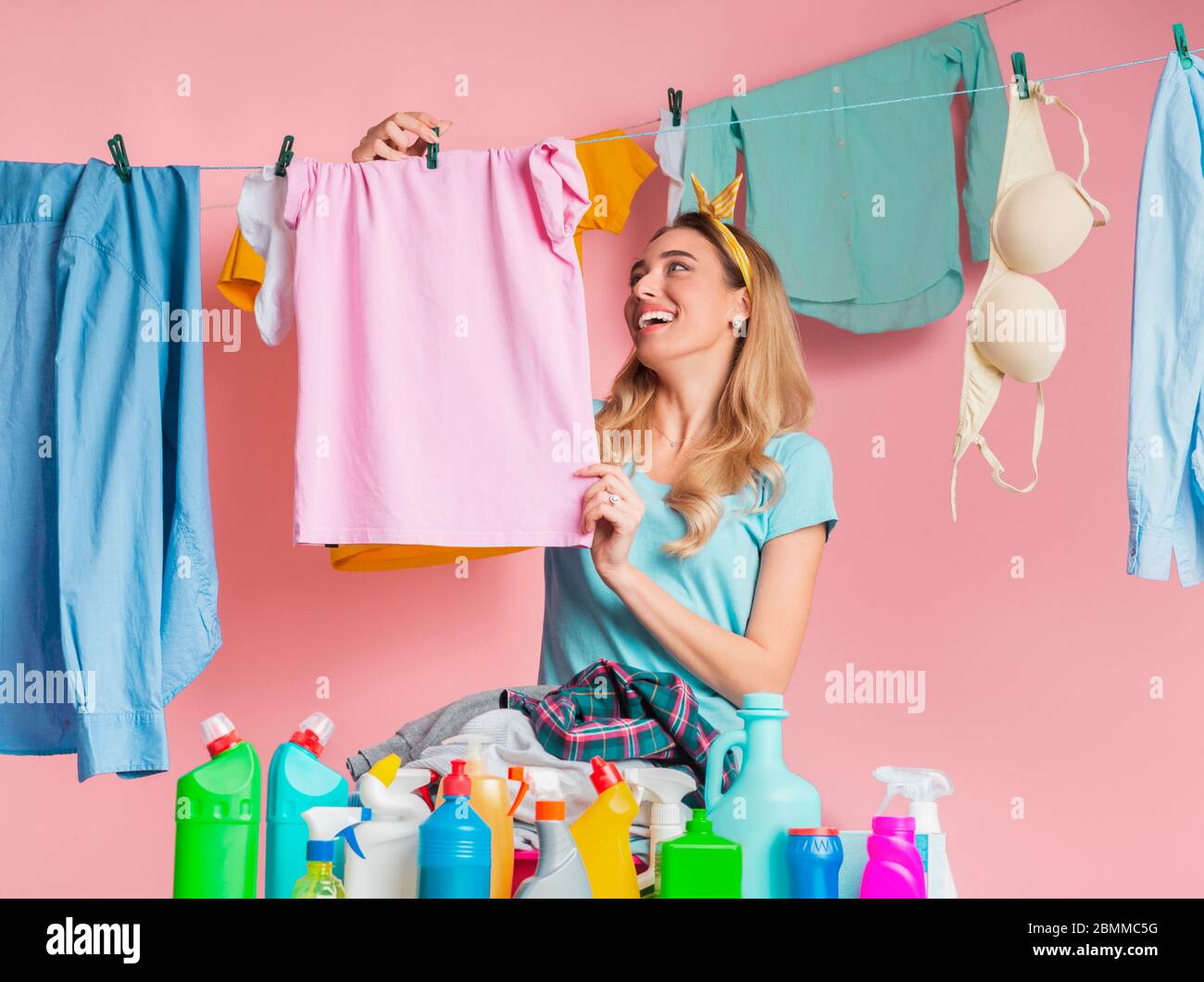 Donna di casa sorridente appendere fuori camicia pulita vicino al prodotto di pulizia con spazio vuoto Foto Stock