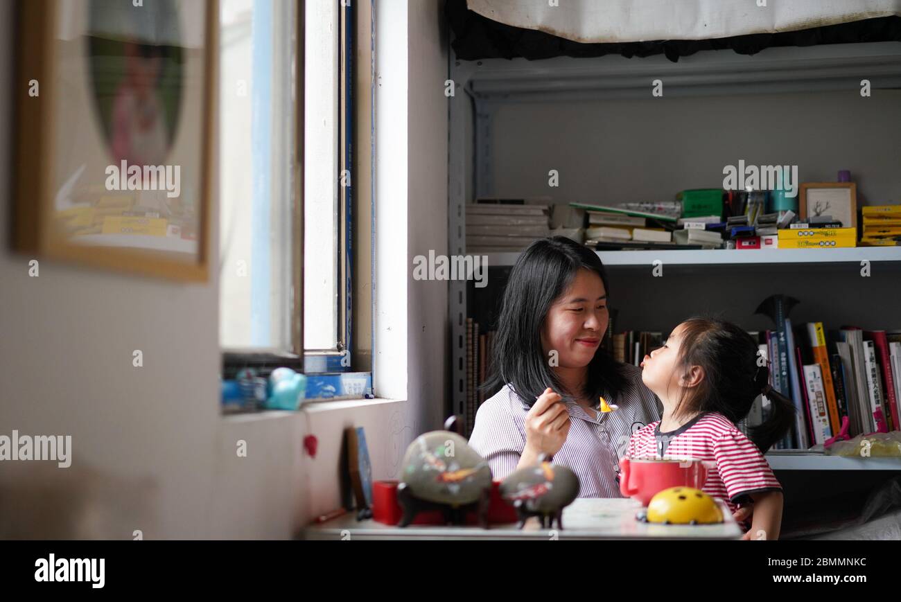 (200510) -- DUCHANG, 10 maggio 2020 (Xinhua) -- Zhang Haijing nutre frutta a sua figlia nel suo studio nella città di Dagang della contea di Duchang, provincia di Jiangxi della Cina orientale, 8 maggio 2020. Zhang Haijing, 30, nato a Lishui, nella provincia di Zhejiang della Cina orientale, fu lasciato in sedia a rotelle dopo un incidente nel 2008. Un anno dopo Zhang trovò il suo interesse nella pittura e cominciò ad imparare il mestiere, il nuovo hobby la aiutò a recuperare gradualmente dal doloroso postumi dell'incidente. Zhang incontrò Dan Yuchao, un uomo che perse la mano destra, nel 2014 e si innamorò rapidamente come loro Foto Stock