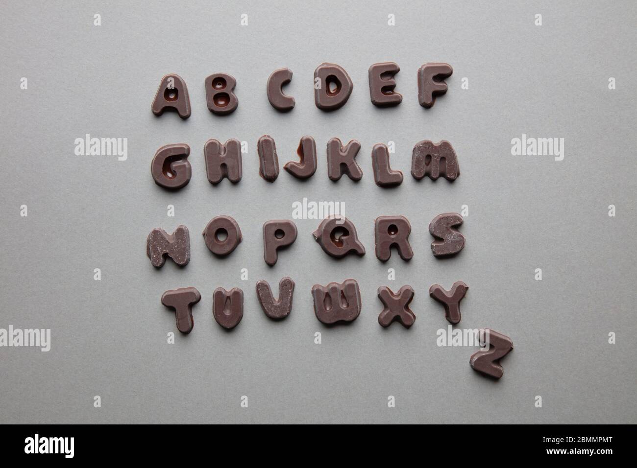 un'immagine artistica di lettere al cioccolato in ordine alfabetico su sfondo grigio Foto Stock