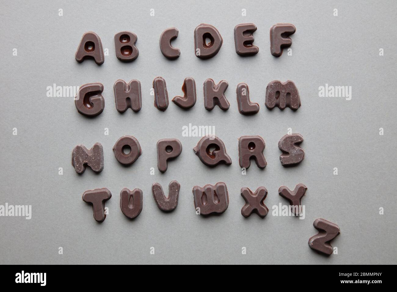 un'immagine artistica di lettere al cioccolato in ordine alfabetico su sfondo grigio Foto Stock