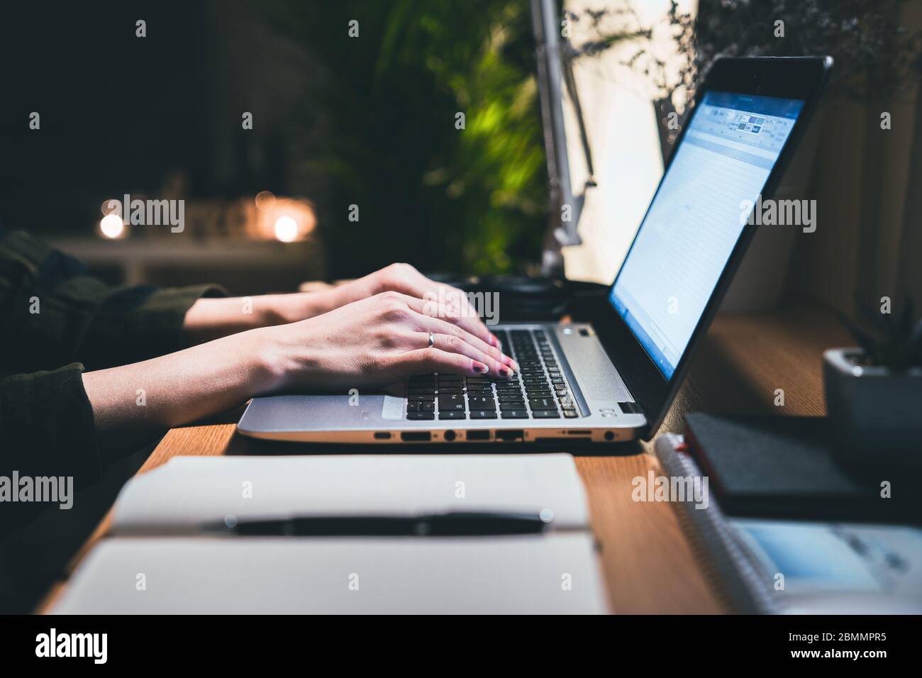 Mani di una donna che utilizza un computer portatile che lavora fuori orario alla sua scrivania in ufficio di notte. Lavora da casa con notebook e penna Foto Stock