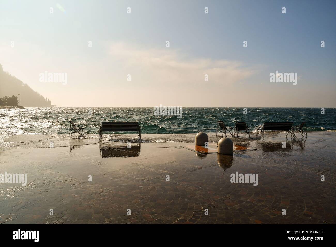 Vista panoramica della riva del lago in una giornata ventosa con alte onde che inondano il vuoto lungomare, Lago di Garda, Verona, Veneto, Italia Foto Stock