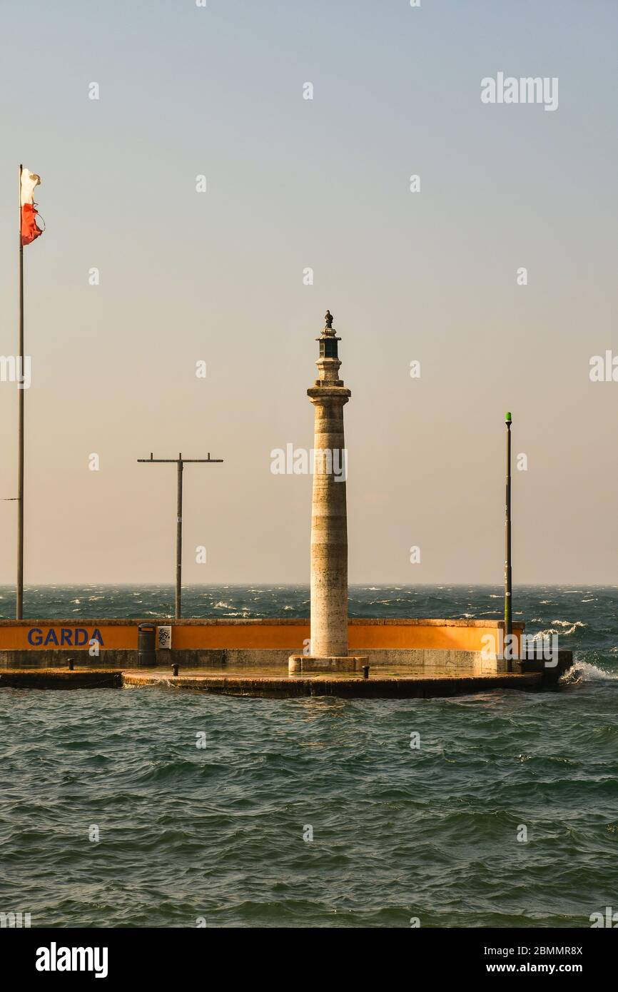 Vista verticale del faro nel porto di Garda sulla riva del Lago di Garda in una giornata soleggiata ventosa con onde alte, provincia di Verona, Veneto, Italia Foto Stock