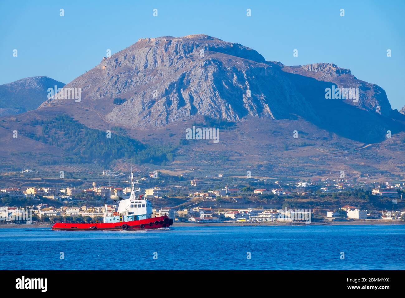 Giornata estiva di sole nel golfo di Corinto. Un rimorchiatore sullo sfondo di una piccola cittadina sulla costa montana. Vista dall'acqua Foto Stock